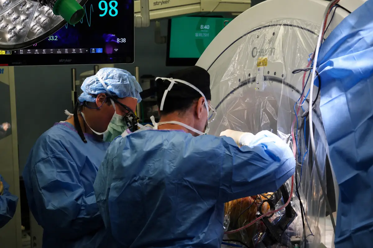 A surgeon working at the stereotactic frame with the draped intraoperative scanner drawn over the patient's head