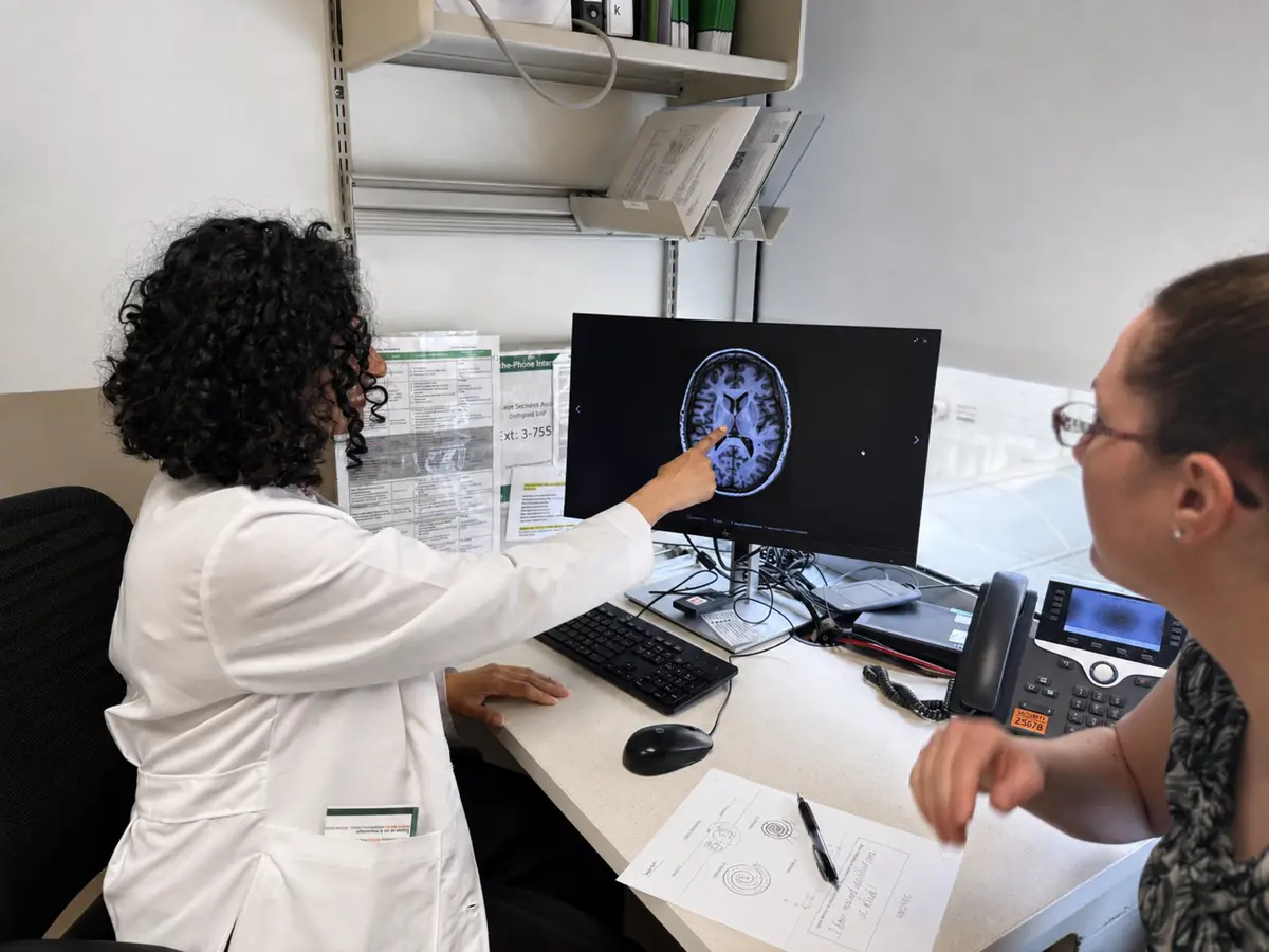 A neurologist pointing to a structure on a brain MRI while the patient follows on the same screen