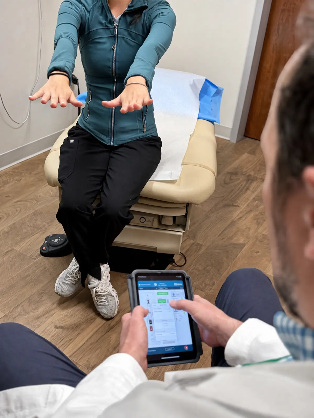 A patient holding both hands outstretched while a clinician adjusts settings on a handheld programmer