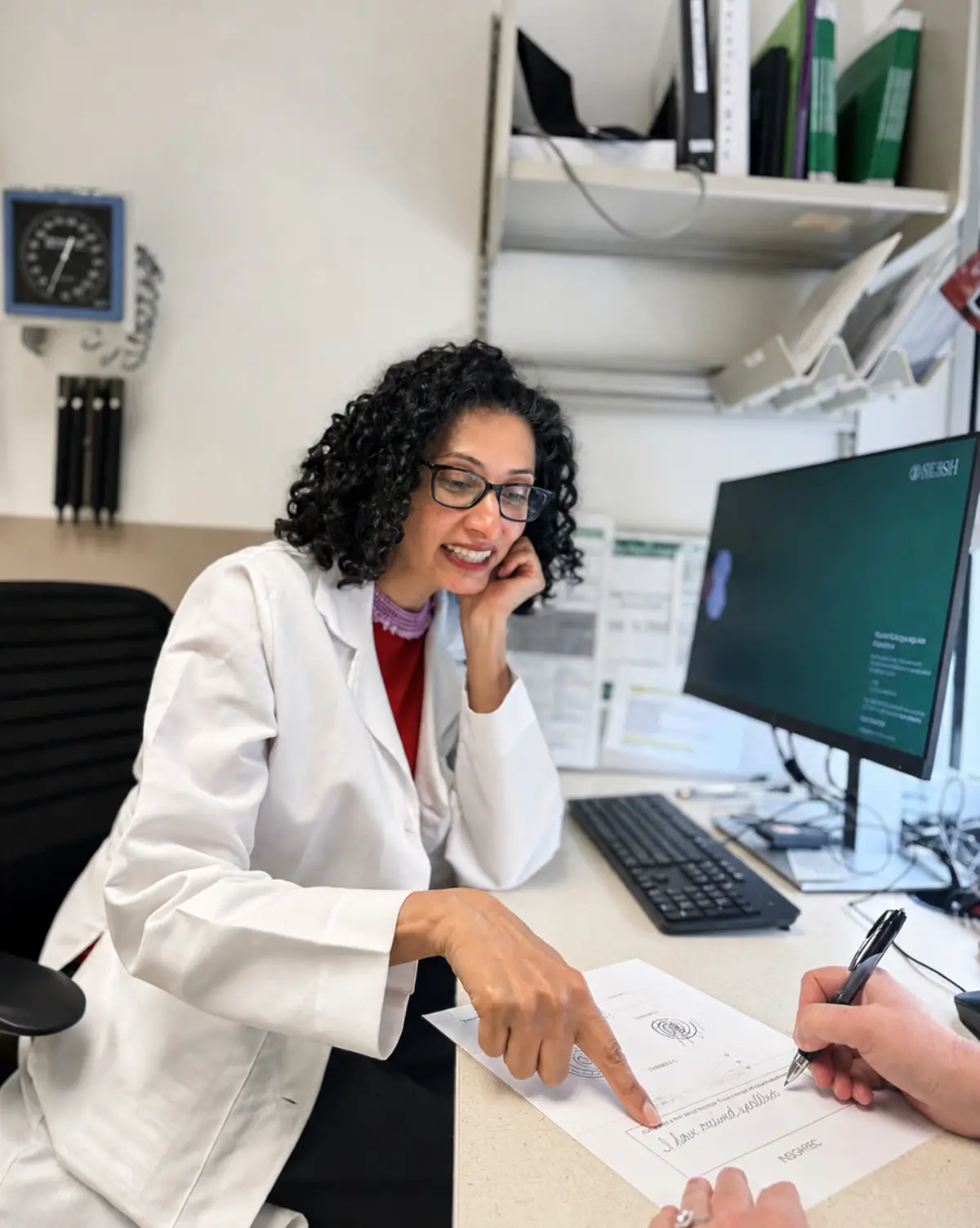 A neurologist pointing to a spiral on a tremor assessment form while the patient fills it in