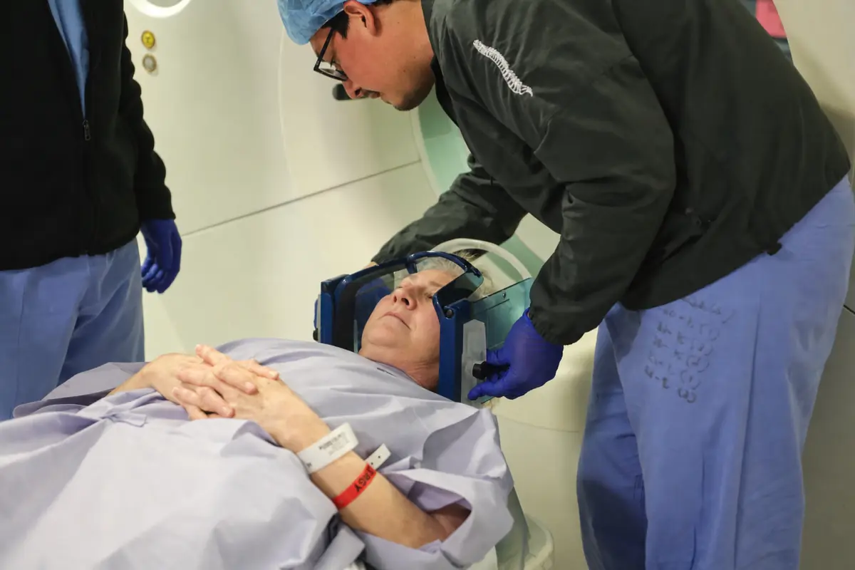 A patient in a stereotactic head frame being positioned for the CT that is merged with their planning MRI, before awake DBS surgery