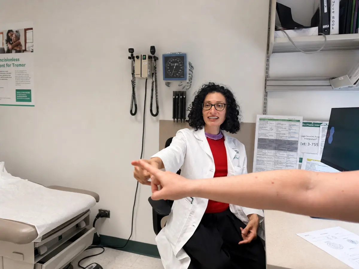 A movement disorders neurologist watching a patient hold an arm outstretched during a tremor examination